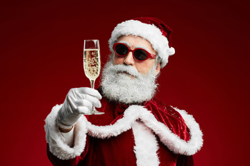 Waist up portrait of modern Santa holding champagne glass while standing over red background, copy space