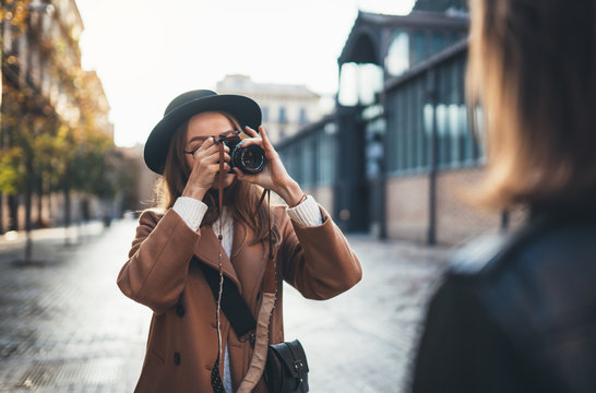 Outdoor smiling lifestyle portrait of pretty young woman having fun in sun city Europe autumn with camera travel photo of photographer Making pictures in glasses and hat with girlfriends