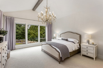 Beautiful bedroom in new luxury home with wood beam and chandelier.