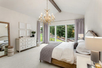 Beautiful bedroom in new luury home. Features chandelier, wood beam on ceiling, and wall of windows.