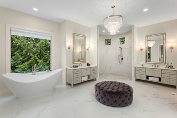 Elegant master bathroom in new luxury home, with two vanities, walk-in shower, soaking tub, and chandelier