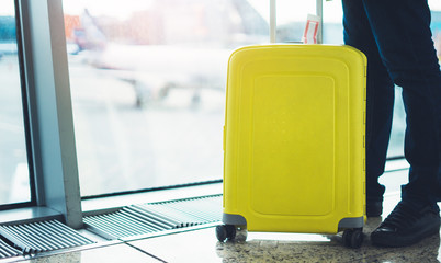 traveler with yellow suitcase backpack at airport on background window blue sky, passenger waiting flight in departure lounge area, hall of ​airport lobby terminal, vacation trip concept