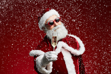 Waist up portrait of cool Santa holding champagne glass while standing over red background with...