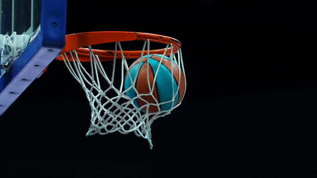 Basketball ring with a net in which the ball flies on a dark background in a sports complex