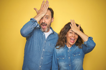 Beautiful middle age couple together standing over isolated yellow background surprised with hand...