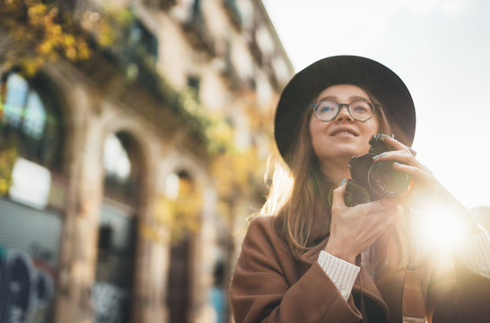 Photographer with retro photo camera. Tourist portrait. Smiling girl in hat travels in Barcelona holiday. Sunlight flare street in europe city. Traveler hipster shooting architecture, space mockup