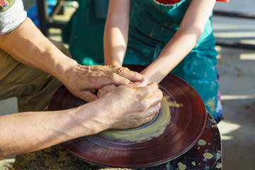 Hands in yellow clay over a rotating Potters wheel sculpt dishes. The master and the disciple