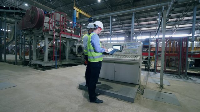Factory male engineers in a modern factory. Workers check factory machines at a modern industrial plant.