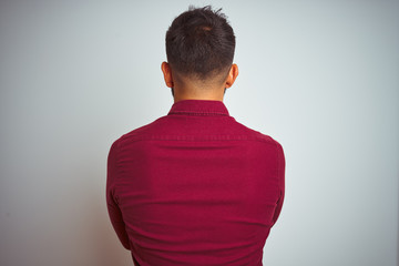 Young indian man wearing red elegant shirt standing over isolated grey background standing...