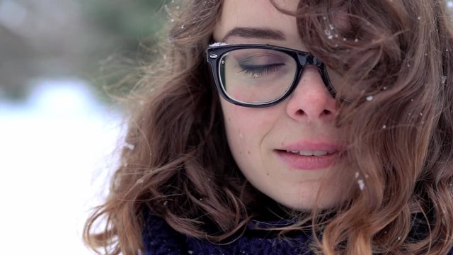 Close-up face of beautiful woman in glasses enjoying snow and wind in her hairs