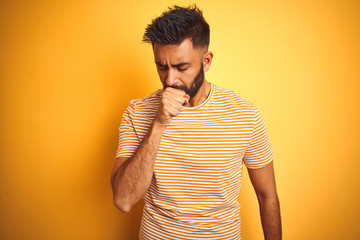 Young indian man wearing t-shirt standing over isolated yellow background feeling unwell and...
