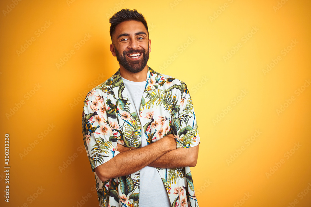 Wall mural Young indian man on vacation wearing summer floral shirt over isolated yellow background happy face smiling with crossed arms looking at the camera. Positive person.