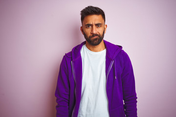 Young indian man wearing purple sweatshirt standing over isolated pink background depressed and worry for distress, crying angry and afraid. Sad expression.