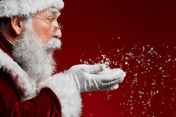 Side view portrait of classic Santa Claus blowing snow while standing against red background, copy...