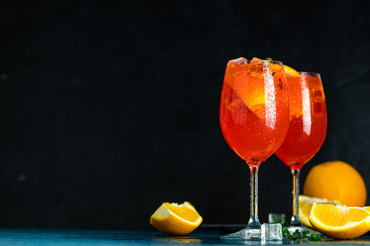 Two Aperol spritz cocktail in big wine glass with oranges, summer Italian fresh alcohol cold drink. Dark bar counter background with tools, summer mood concept, selective focus