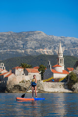 Summer holidays vacation travel. SUP Stand up paddle board. Young woman sailing on beautiful calm lagoon along Budva old town