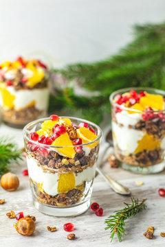Greek yogurt with granola, orange and pomegranate berries for healthy breakfast on light gray wooden table, copy space