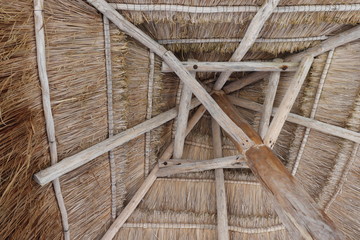 beach umbrella made of straw held by wooden pole seen from below.