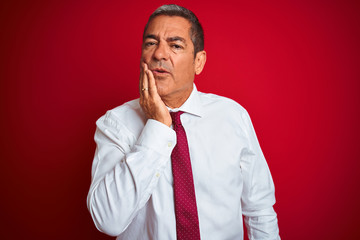 Handsome middle age businessman standing over isolated red background touching mouth with hand with painful expression because of toothache or dental illness on teeth. Dentist concept.