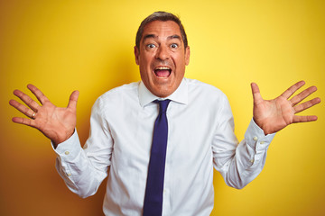 Handsome middle age businessman standing over isolated yellow background celebrating crazy and amazed for success with arms raised and open eyes screaming excited. Winner concept