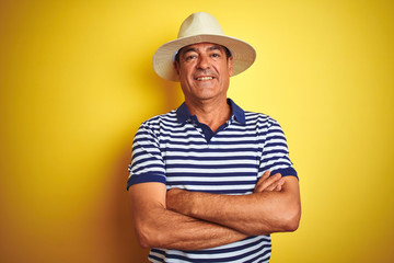 Handsome middle age man wearing striped polo and hat over isolated yellow background happy face smiling with crossed arms looking at the camera. Positive person.