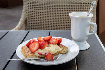 Coffee and dessert on a cafe street terrace. Cup of coffee and fruit cake with strawberries on a wooden table close-up.