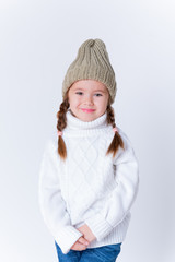 Little girl in knitted sweater and hat posing in studio. Winter fashion