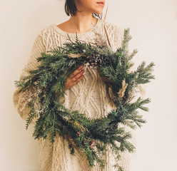 Girl in knitted sweater holding stylish rustic wreath. Hipster girl with rural modern wreath on...