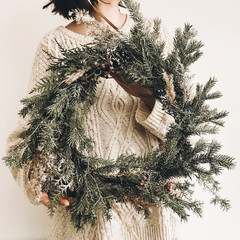 Girl in knitted sweater holding stylish rustic wreath. Hipster girl with rural modern wreath on...