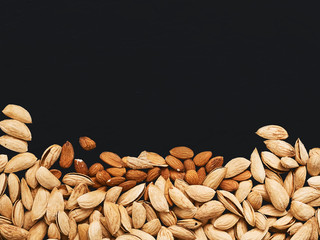 Natural organic almonds are scattered on a black background. Top view, copy space. Healthy eating concept. Natural light.