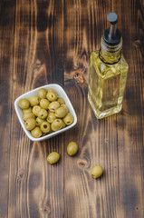 Glass bottle of olive oil and olive in a white bowl on a wooden background. Top view. Organic olive oil concept