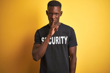 African american safeguard man wearing security uniform over isolated yellow background asking to be quiet with finger on lips. Silence and secret concept.