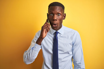 African american businessman talking on smartphone standing over isolated yellow background scared in shock with a surprise face, afraid and excited with fear expression