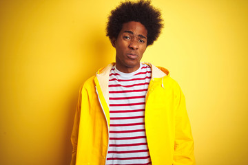 African american man with afro hair wearing rain coat standing over isolated yellow background...