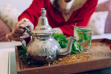 Unrecognizable arabic woman holding a hot arab silver teapot. Moroccan green herbal tea poured in...
