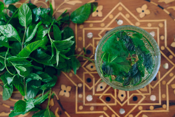 Hot or cold peppermint herbal arab tea and fresh mint leafs on a decorated muslim tray at home. Detail from above of a traditional beverage. Moroccan green herbal tea poured in traditional ways.