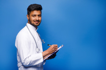 Portrait of a indian male doctor holding a blank clipboard and looking at him. Copy space.