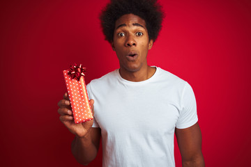 Young african american man holding valentine gift standing over isolated red background scared in shock with a surprise face, afraid and excited with fear expression
