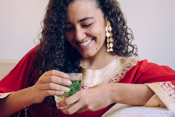 Beautiful young ethnic woman drinking herbal tea at home. Moroccan female with traditional clothes...