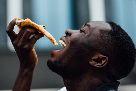 Fototapeta Young man eats a piece of appetizing pizza. Hungry guy holds a piece of pizza in his hands, looks at him and is going to eat it. Fast food.