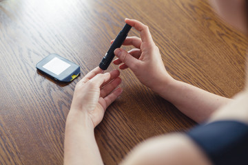Woman using lancet to take blood sample to check glucose level with traditional glucometer