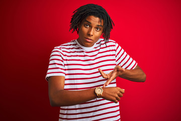 Young afro man with dreadlocks wearing striped t-shirt standing over isolated red background In...