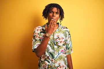 Afro man with dreadlocks on vacation wearing summer shirt over isolated yellow background bored yawning tired covering mouth with hand. Restless and sleepiness.
