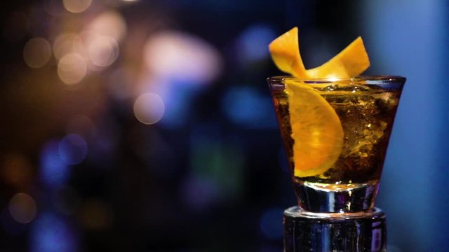 Brazilian drink cock-tail rotating with bar background in blue color. Old fashioned glass. Fixed plane.