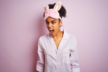 Young african american woman wearing pajama and mask over isolated pink background angry and mad screaming frustrated and furious, shouting with anger. Rage and aggressive concept.