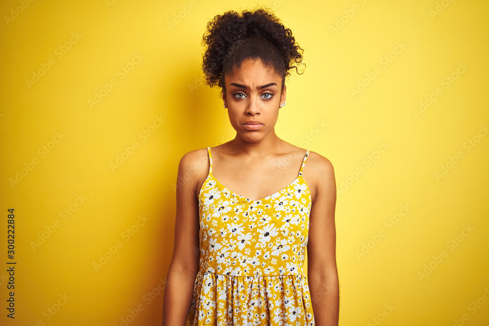 Sticker African american woman wearing casual floral dress standing over isolated yellow background depressed and worry for distress, crying angry and afraid. Sad expression.