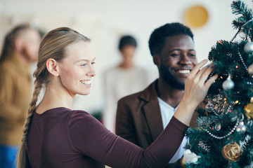 Portrait of beautiful young woman looking at decorations on Christmas tree during party banquet, copy space