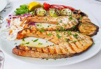 Sliced swordfish grilled with grilled vegetables like eggplant, zucchini and pepper, sprinkled with chopped parsley leaves. Closeup view.