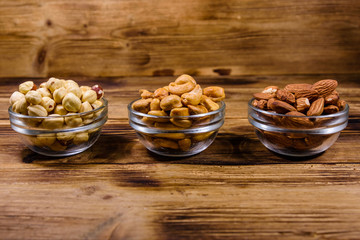 Various nuts (almond, cashew, hazelnut) in glass bowls on a wooden table. Vegetarian meal. Healthy eating concept