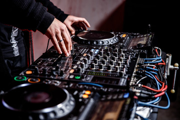 DJ plays live set and mixing music on turntable console at stage in the night club. Disc Jokey Hands on a sound mixer station at club party. DJ mixer controller panel for playing music and partying.